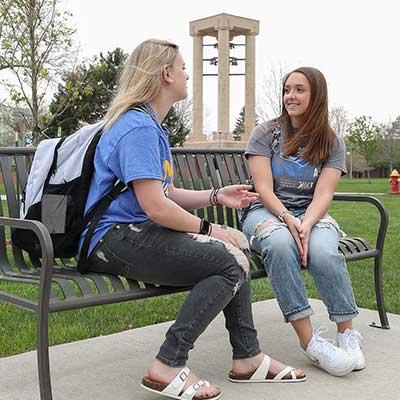 two students chat on a park bench